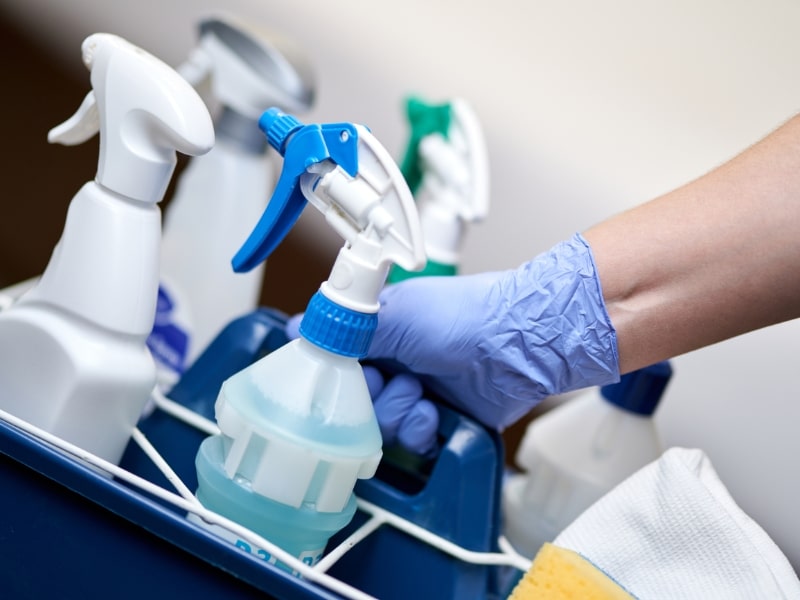 Gloved hand holding caddy of the best cleaning supplies and disinfectant sprays