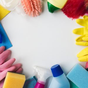 Flat lay of essential wholesale cleaning supplies including rubber gloves, spray bottles, and colorful sponges on a white background.
