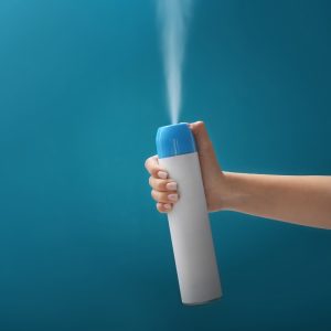 Hand spraying an aerosol air freshener can with a blue cap against a solid blue background.
