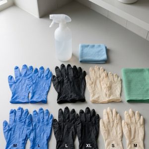 Different sizes and thicknesses of disposable cleaning gloves arranged beside commercial cleaning supplies on a clean surface.